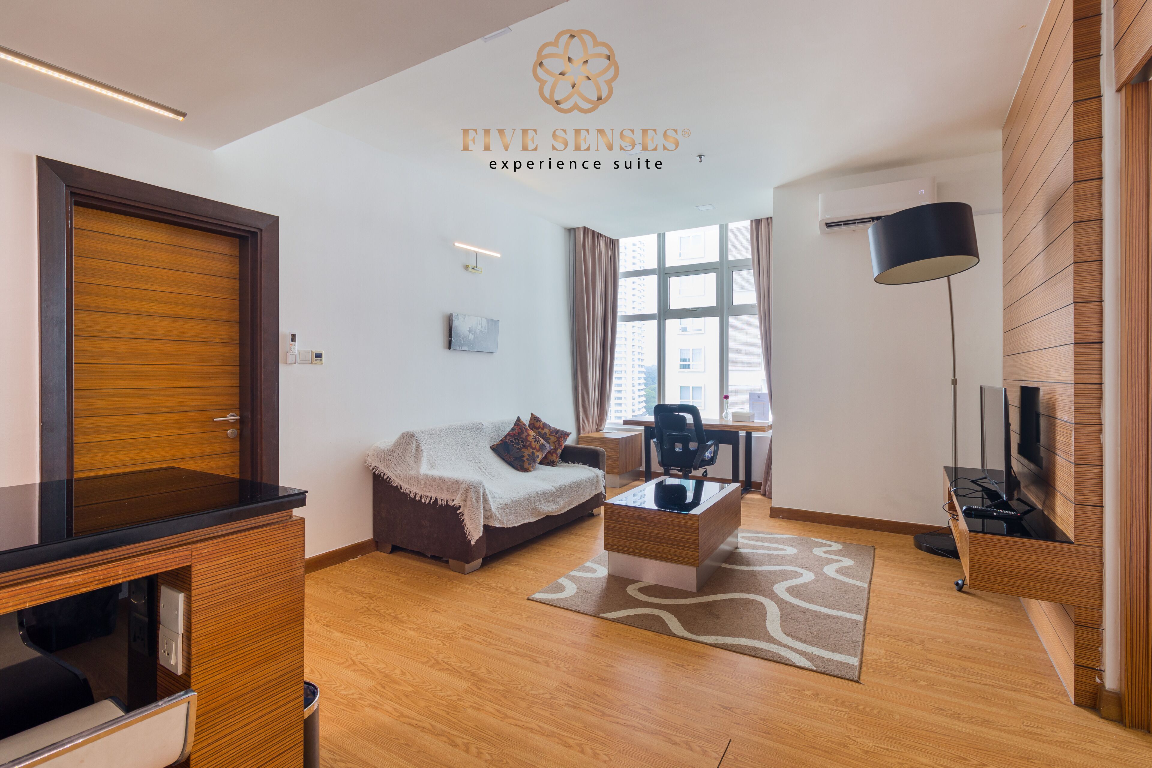Una sala de estar moderna con sofá, mesa de centro y mueble para televisión. Hay una ventana con cortinas, una lámpara y un equipo de aire acondicionado instalado en el techo.
