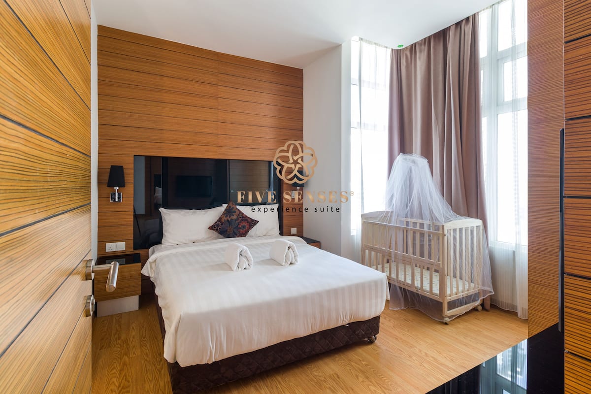 Ein Hotelzimmer mit einem großen Bett, einem Babybett, Holzvertäfelung, einem Nachttisch und einem Fenster mit Vorhängen.