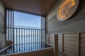 Une salle de spa en bois dotée d’une grande fenêtre donnant sur la mer, d’un banc en bois et d’une fenêtre circulaire ornée d’un motif décoratif.