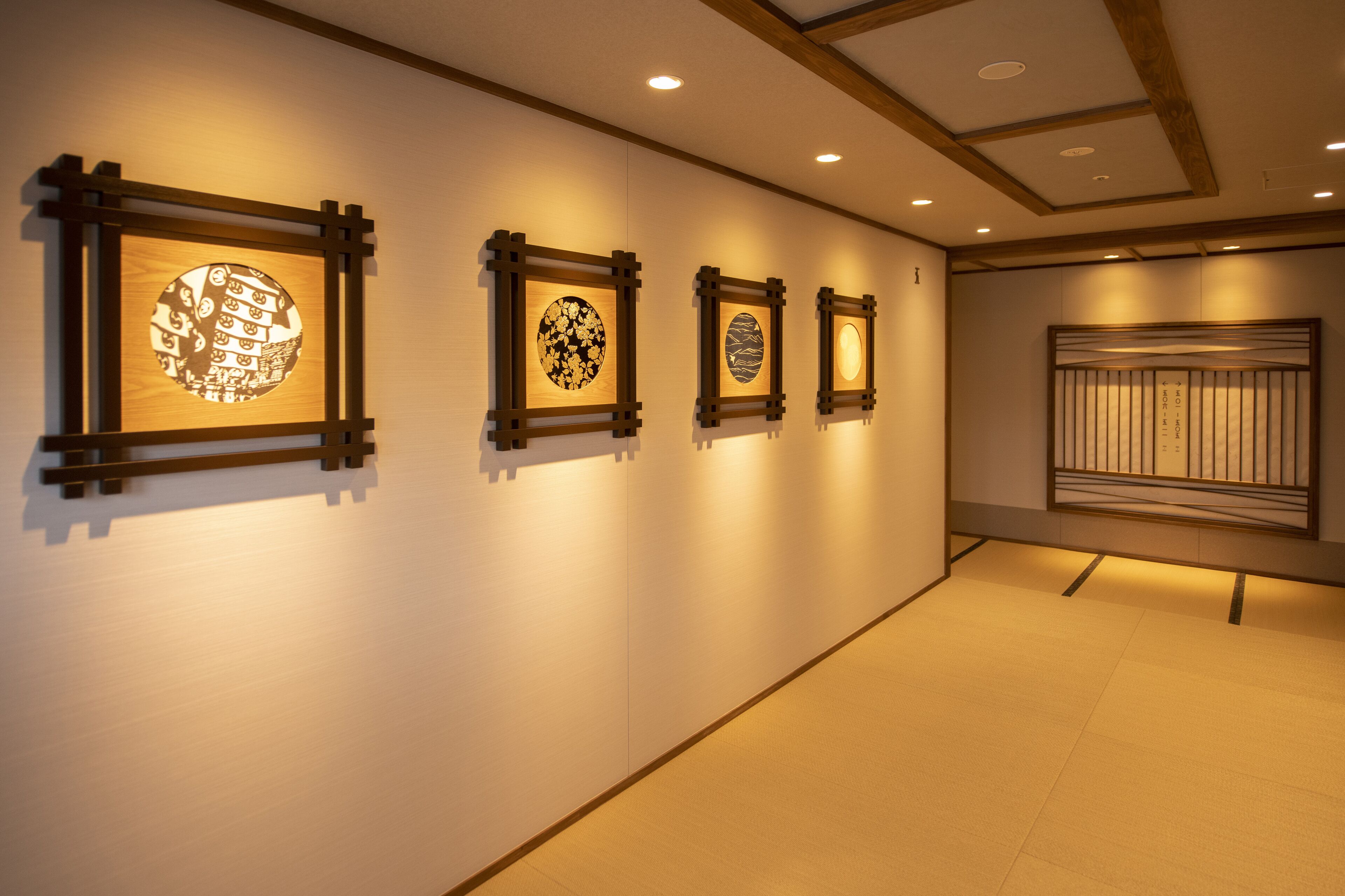 A hallway with four framed artworks on the wall, a wooden panel with vertical slats, and a tiled floor.