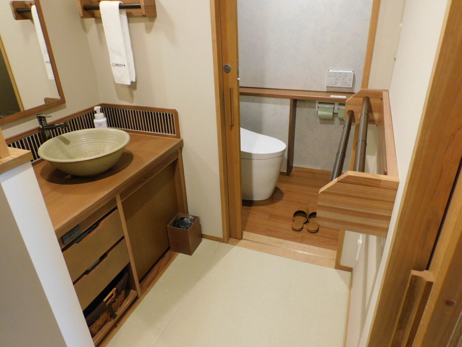Un baño compacto con tocador de madera, un lavamanos grande, un inodoro y un pequeño cubo de basura.
