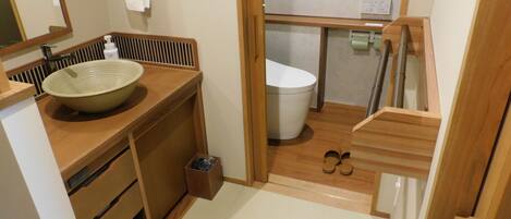 Un baño compacto con tocador de madera, un lavamanos grande, un inodoro y un pequeño cubo de basura.