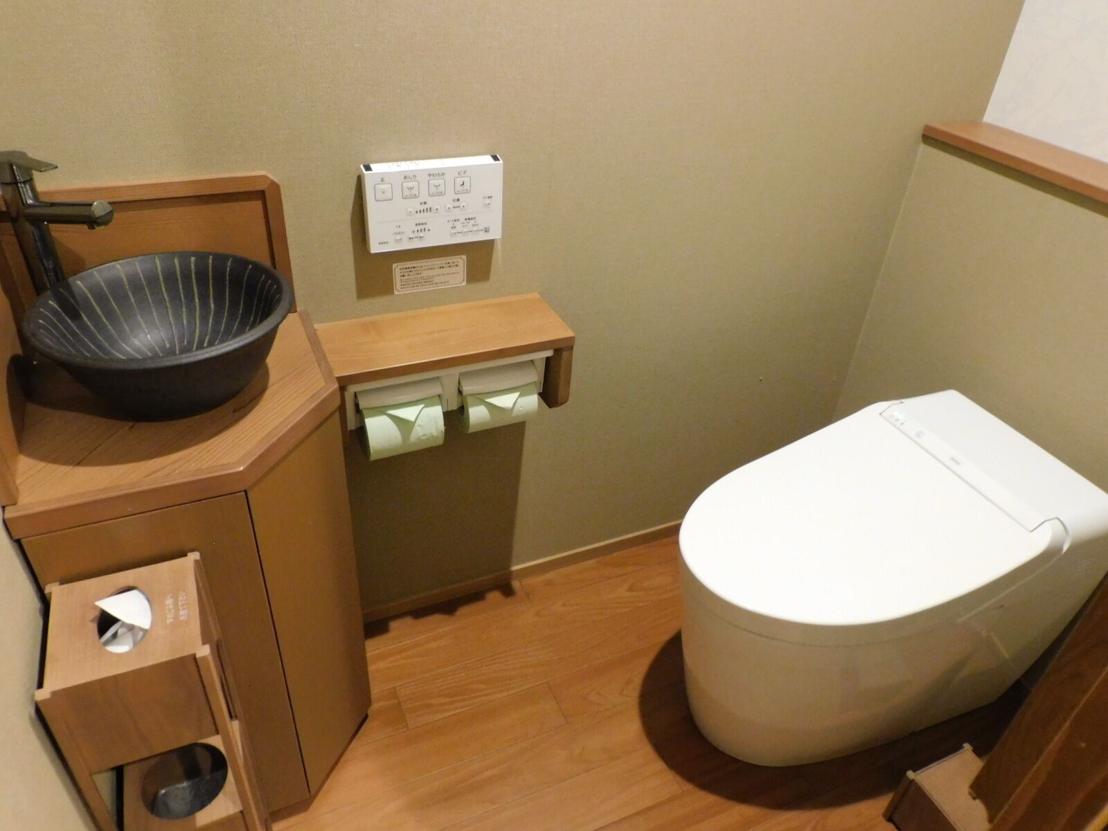 A compact bathroom with a toilet, a sink with a black basin, and a small trash bin with a white lid.