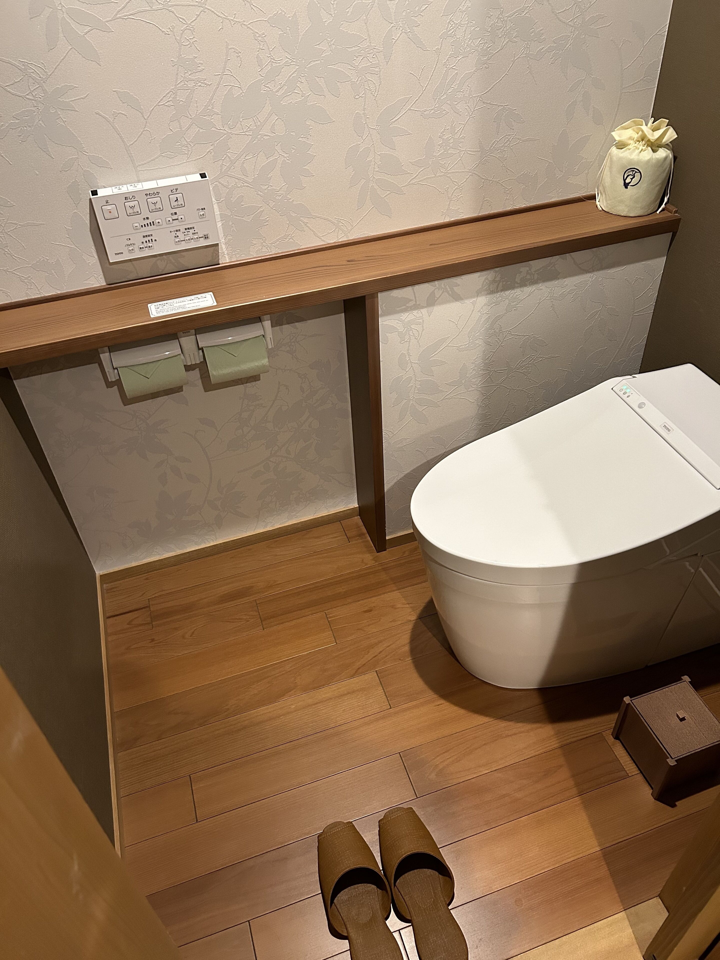 A bathroom with a wooden vanity, a toilet, and a pair of shoes on the floor.