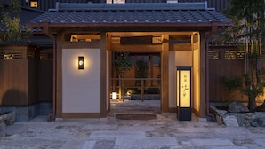 Un bâtiment japonais traditionnel, avec un toit recouvert de tuiles, une porte d’entrée en bois et un sol en pierre.