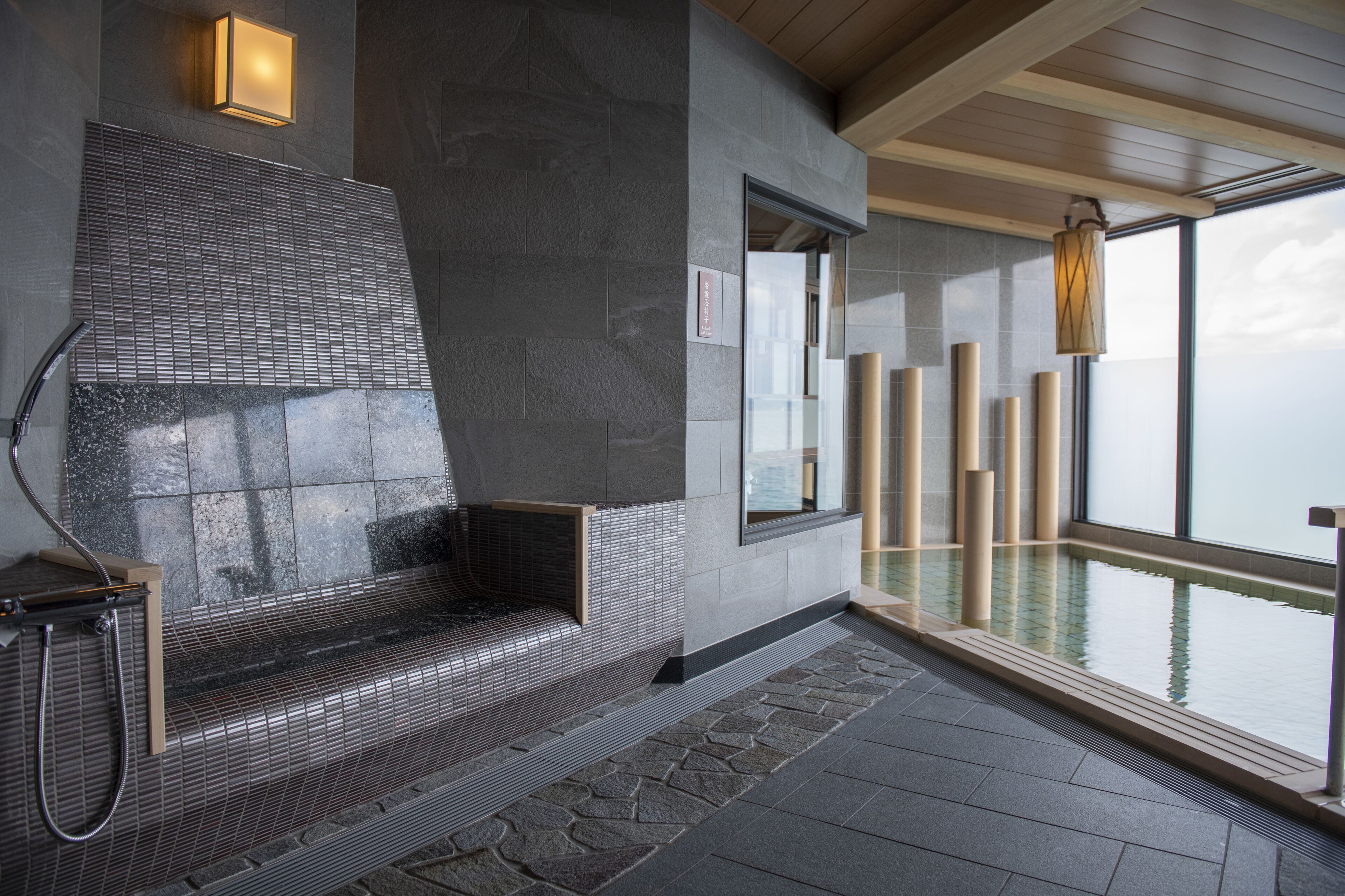 Un espace spa moderne avec un banc en pierre, un mur de verre et une vue sur l’eau.