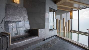 Un espace spa moderne avec un banc en pierre, un mur de verre et une vue sur l’eau.