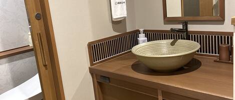A bathroom with a wooden vanity, a large ceramic sink, a mirror, and a towel hanging on a wooden rack.