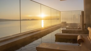 Un espace intérieur paisible avec un élément aquatique, agrémenté de marches menant à un bassin où l'on peut admirer le reflet du soleil couchant sur une étendue d'eau.