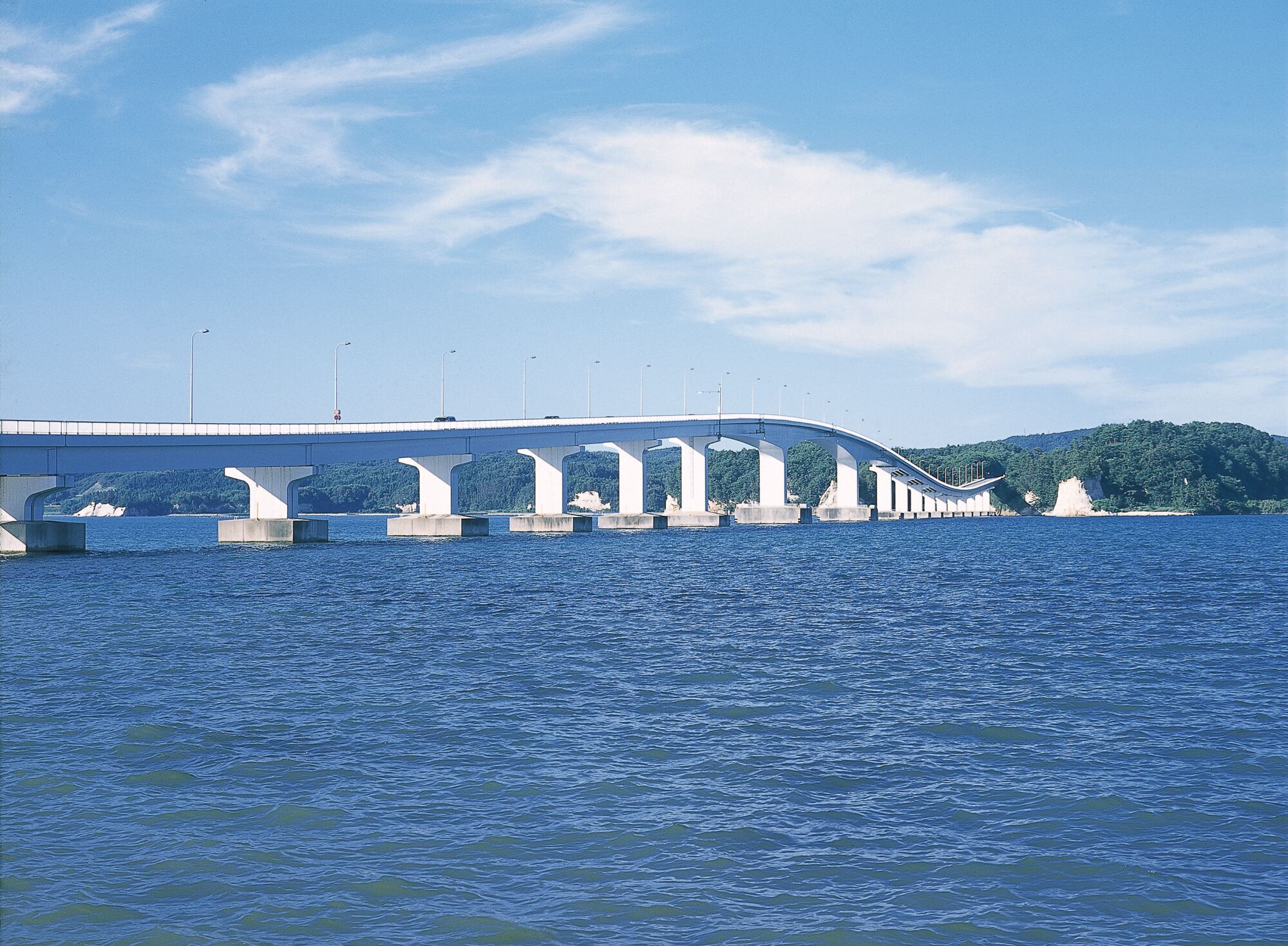 A large bridge spanning a body of water with multiple support pillars and a clear sky.