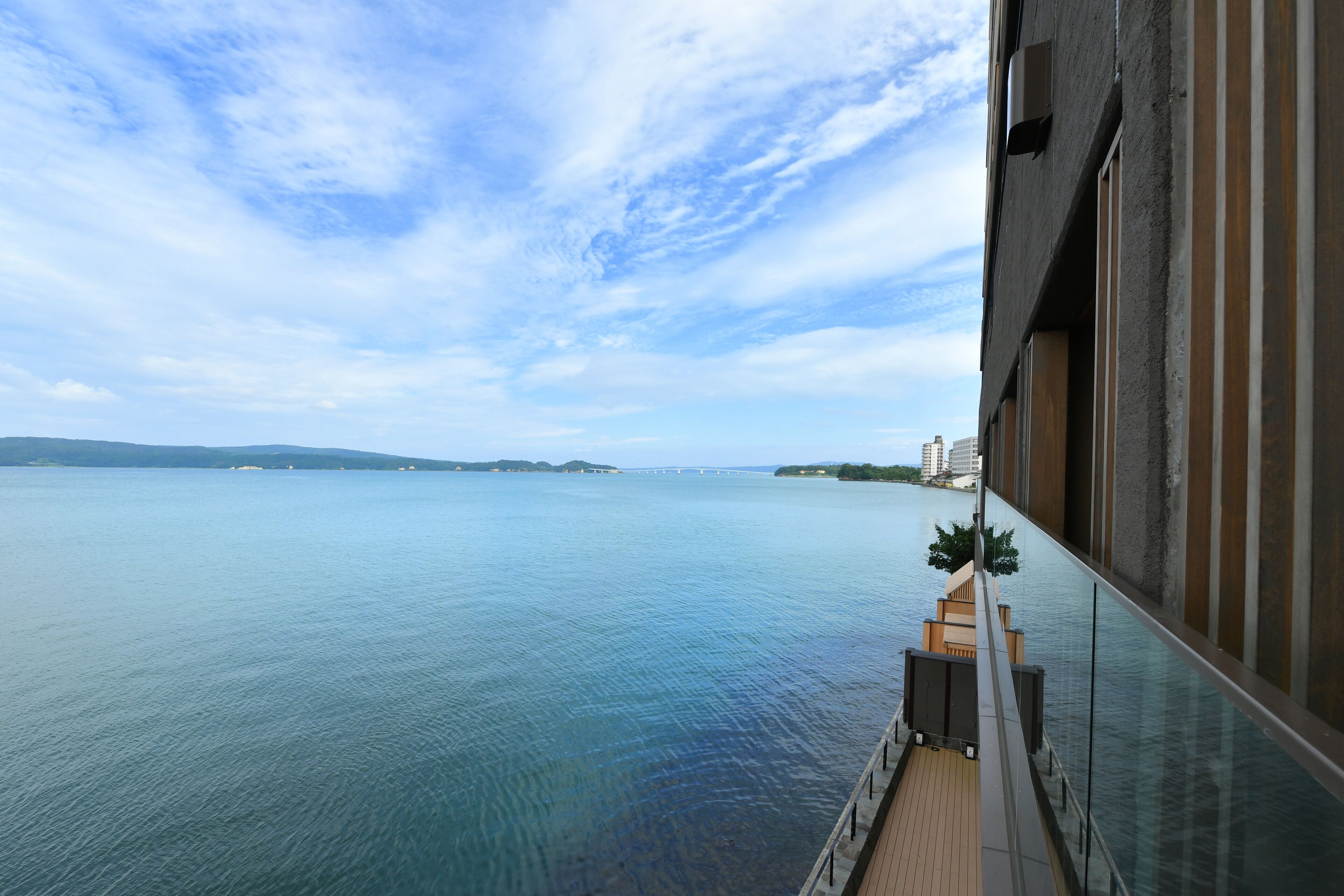 A balcony with a view of a calm body of water, a distant bridge, and a clear sky.
