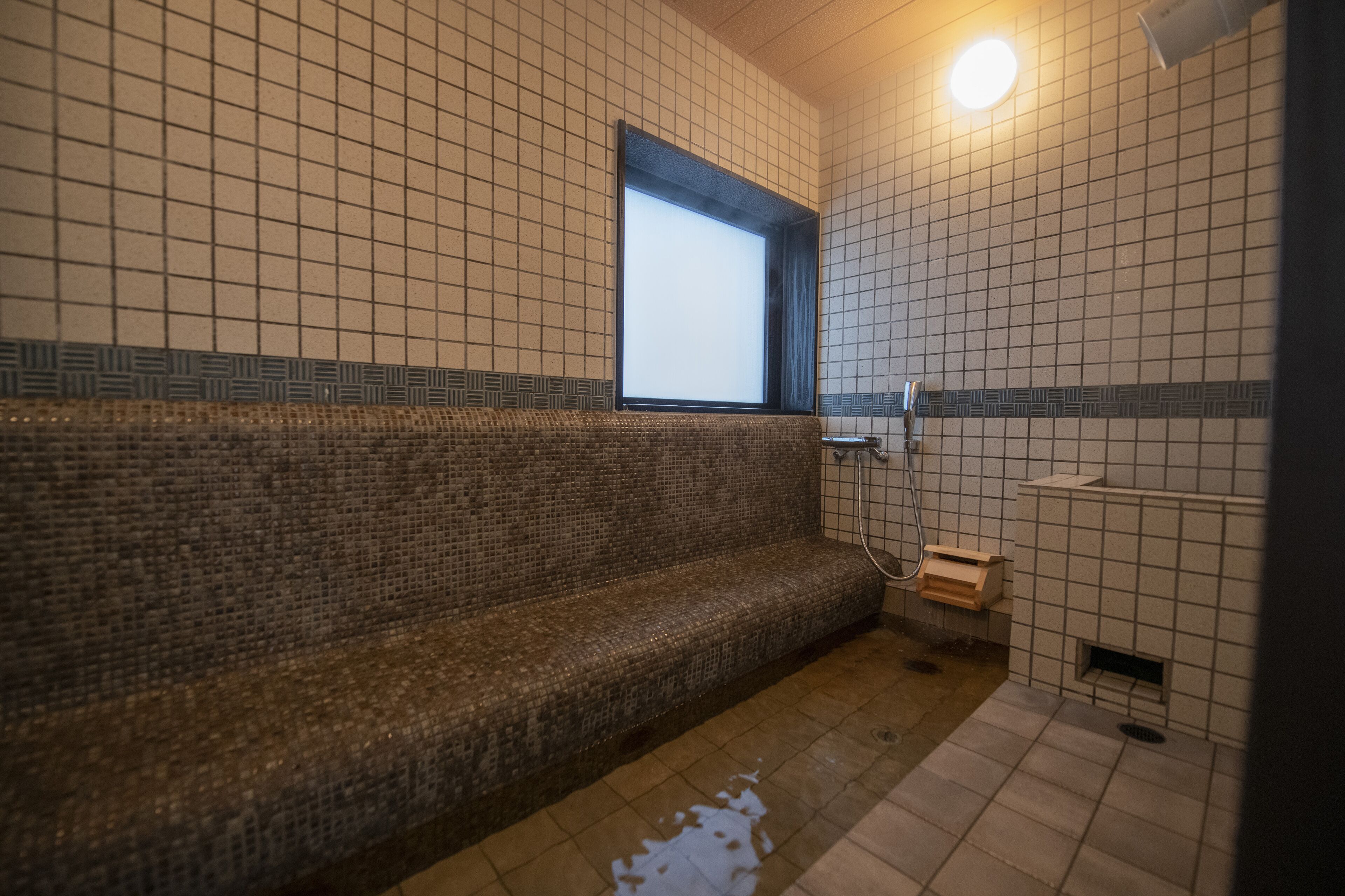 A tiled bathroom with a bench, a window, and a shower area.