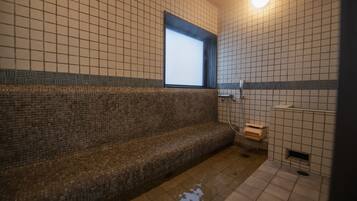 A tiled bathroom with a bench, a window, and a shower area.