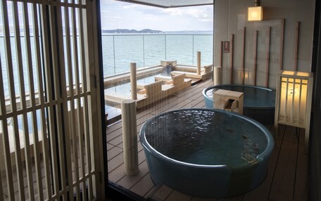 A hot tub area with a view of the sea, wooden deck, and a lantern.