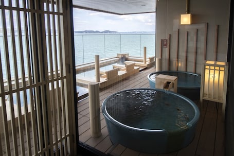 A hot tub area with a view of the sea, wooden deck, and a lantern.