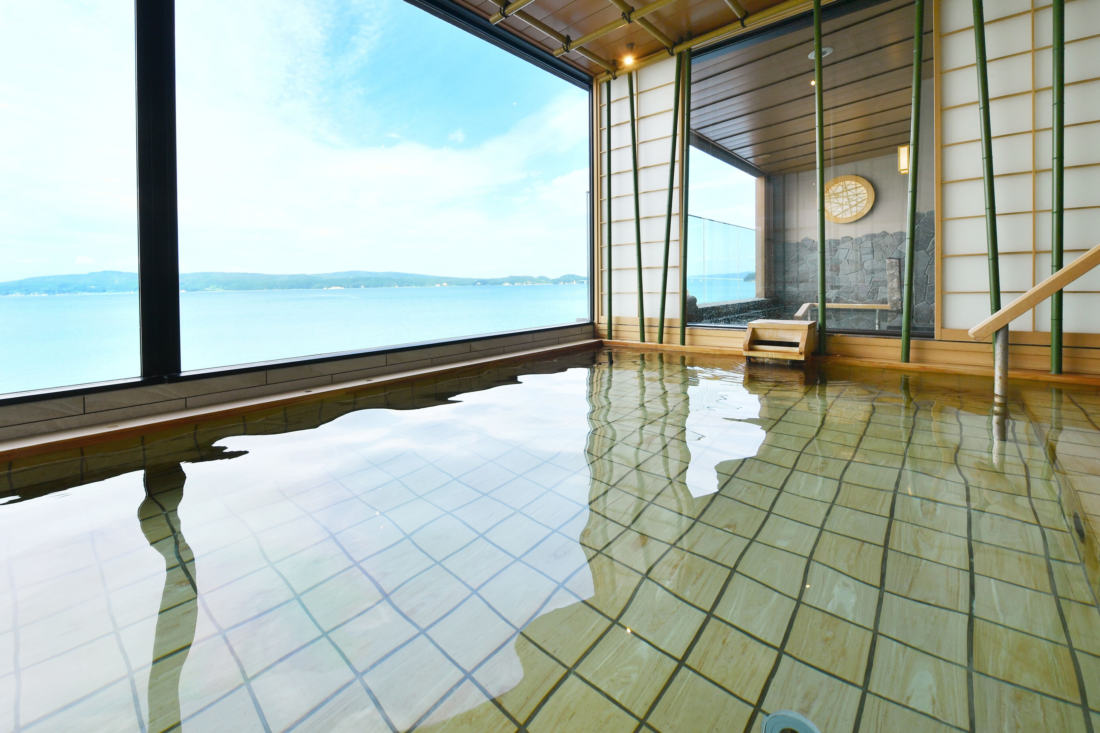 Un onsen japonais traditionnel offrant une vue sur la mer, avec un mur de pierre et un banc en bois.