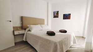 Un dormitori amb un llit, una tauleta de nit, una làmpada penjada a la paret i dos quadres.