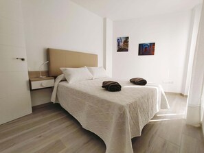 A bedroom with a bed, a nightstand, a wall-mounted lamp, and two paintings.