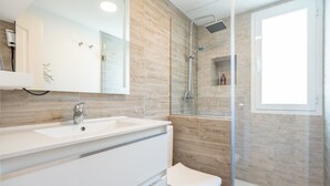 Et moderne badeværelse med hvid vask, spejl og glasbrusekabine.