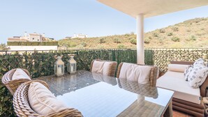 En udendørs terrasse med et bord med glasplade, fletstole og en polstret sofa.