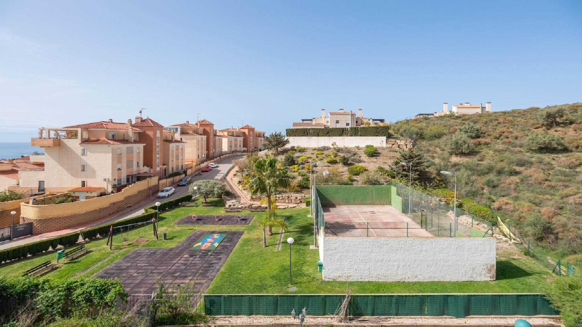 Zona residencial con casas adosadas, una calle pavimentada y una cancha deportiva verde.
