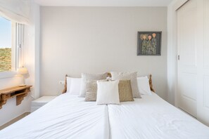 A bedroom with a bed, pillows, a bedside table, a lamp, and a painting on the wall. - Renthas Cumbres de Golf (Rincon De La Victoria)