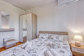 A bedroom with a bed, bedside table, lamp, wardrobe, and an air conditioning unit. - Sea Breeze Residence Mariella, Umag, Croatia (Umag)