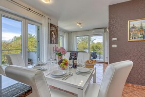 Un comedor con una mesa blanca dispuesta para cuatro personas, un frutero, botellas de vino y una cesta de pan.