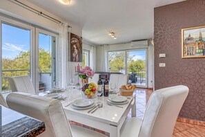 Un coin repas avec une table dressée pour quatre personnes, un vase de fleurs et une bouteille de vin.