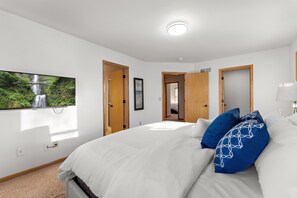 A bedroom with a large bed, a TV mounted on the wall, and a view of a waterfall through the window.