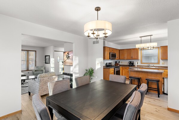 A modern kitchen with wooden cabinets, a central island, and a dining area with a dark wooden table and grey upholstered chairs.