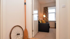 A hallway with a wooden floor, a door leading to a living area with a sofa and a lamp, and a window with patterned curtains. - Pedals and Paddles, waterfront (Dunoon)