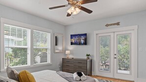 Une chambre à coucher avec un lit, une commode, un ventilateur de plafond et un tableau représentant un paysage urbain.