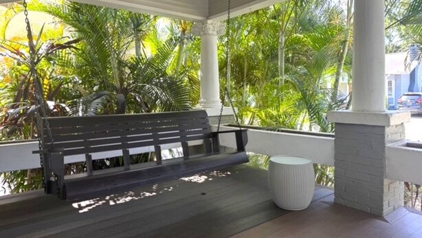 Un porche abrité avec un banc, des colonnes et un pot de fleurs.
