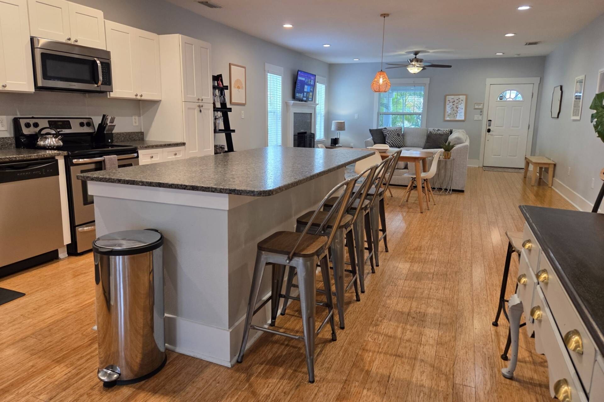 A modern kitchen with a central island, bar stools, stainless steel appliances, and a dining area with a sofa and table.