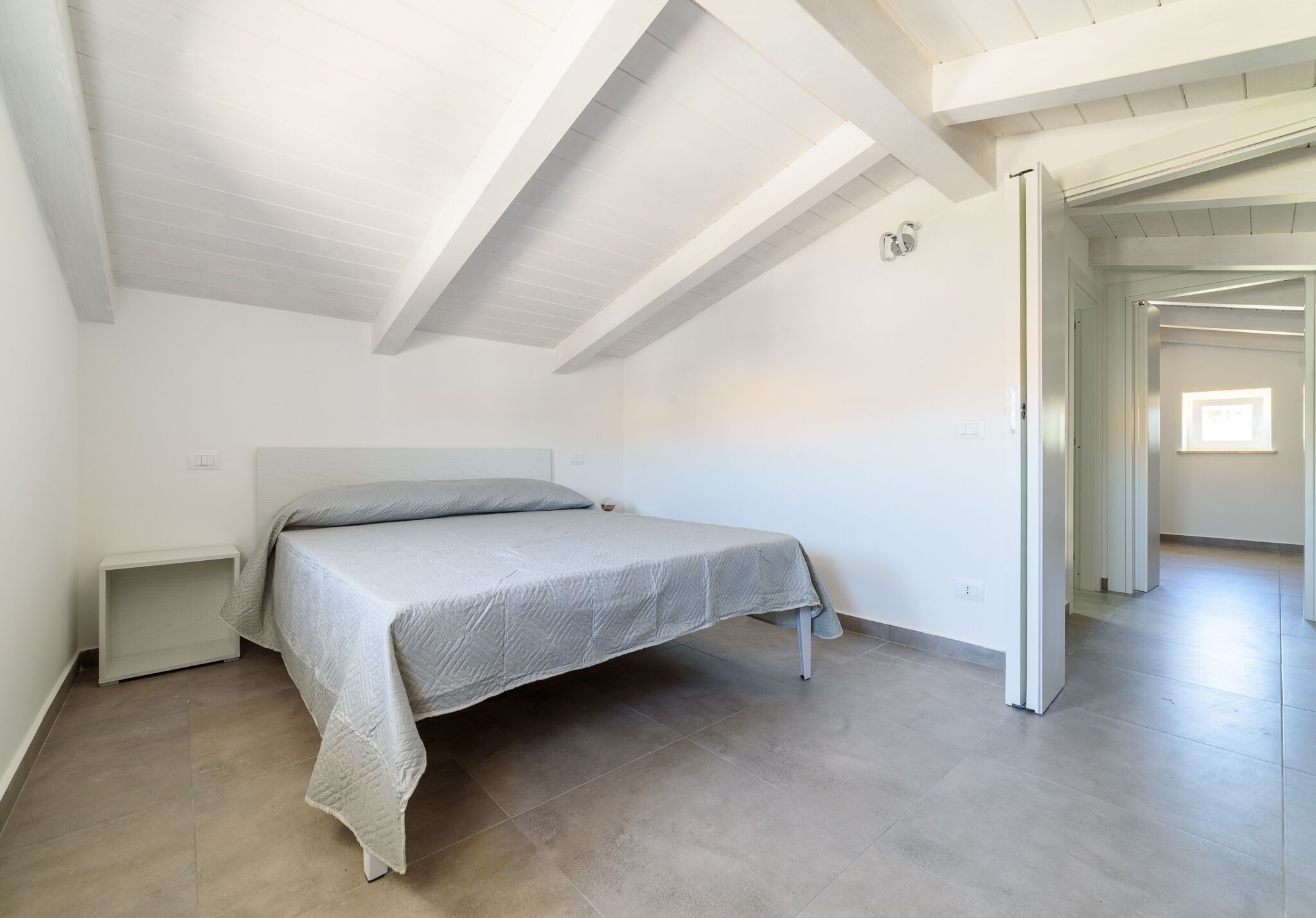 Un dormitorio con cama, mesita de noche y techo con vigas a la vista.