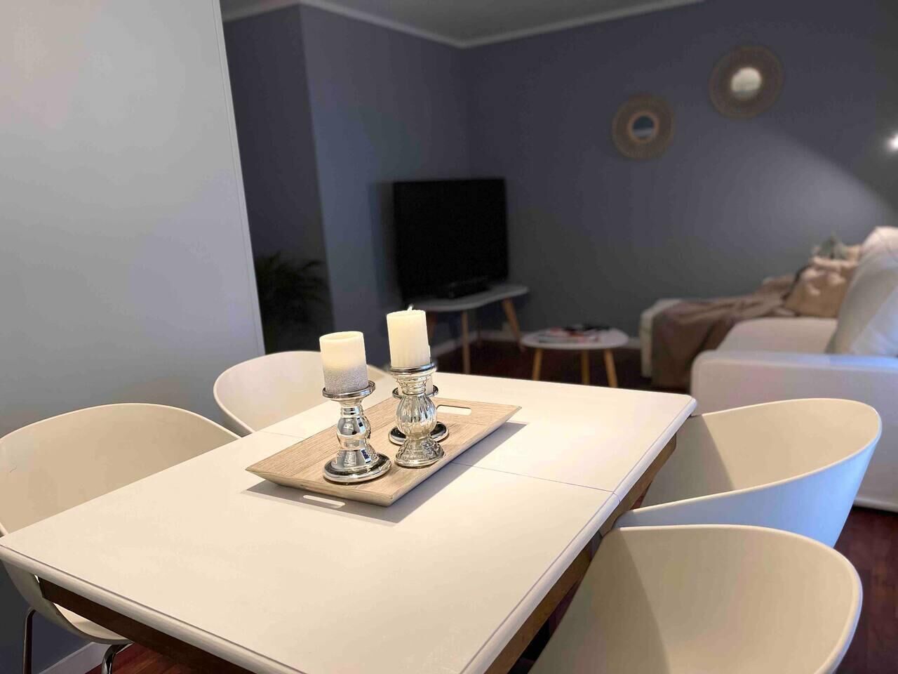 A modern living room with a dining table set for two, featuring white chairs and a tray with candles.