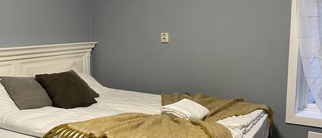 A bed with white bedding and a brown throw blanket, a white headboard, and a window with a curtain.