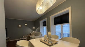A dining area with a white table set for four, a chandelier, and a window with blinds. - Charming 2-Bed Apartment in Stavanger (Stavanger)