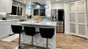 Uma cozinha moderna com uma ilha central, banquetas, iluminação pendente e uma geladeira.