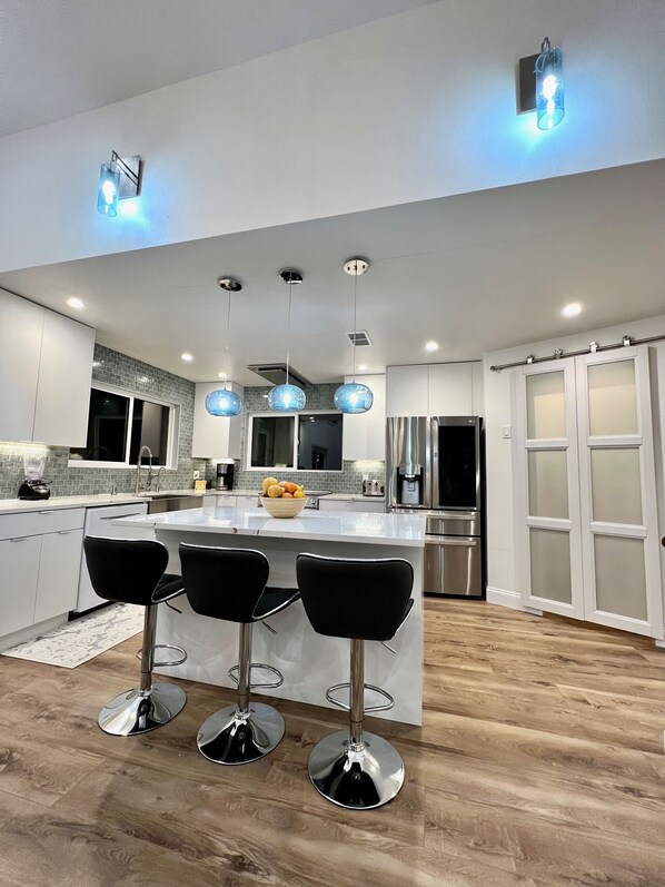 Une cuisine moderne dotée d’un îlot central, de tabourets de bar, de luminaires suspendus et d’un réfrigérateur.