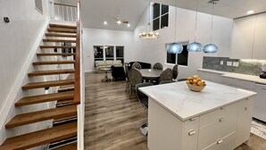 Cozinha moderna com ilha central, escada de madeira e ilumina ção pendente.