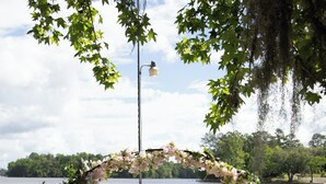 Um cais de madeira com um arco floral que leva a uma mesa montada para uma cerimônia de casamento à beira de um lago.