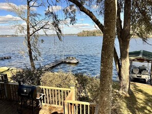 A lakeside deck with a grill, dock, and boat.