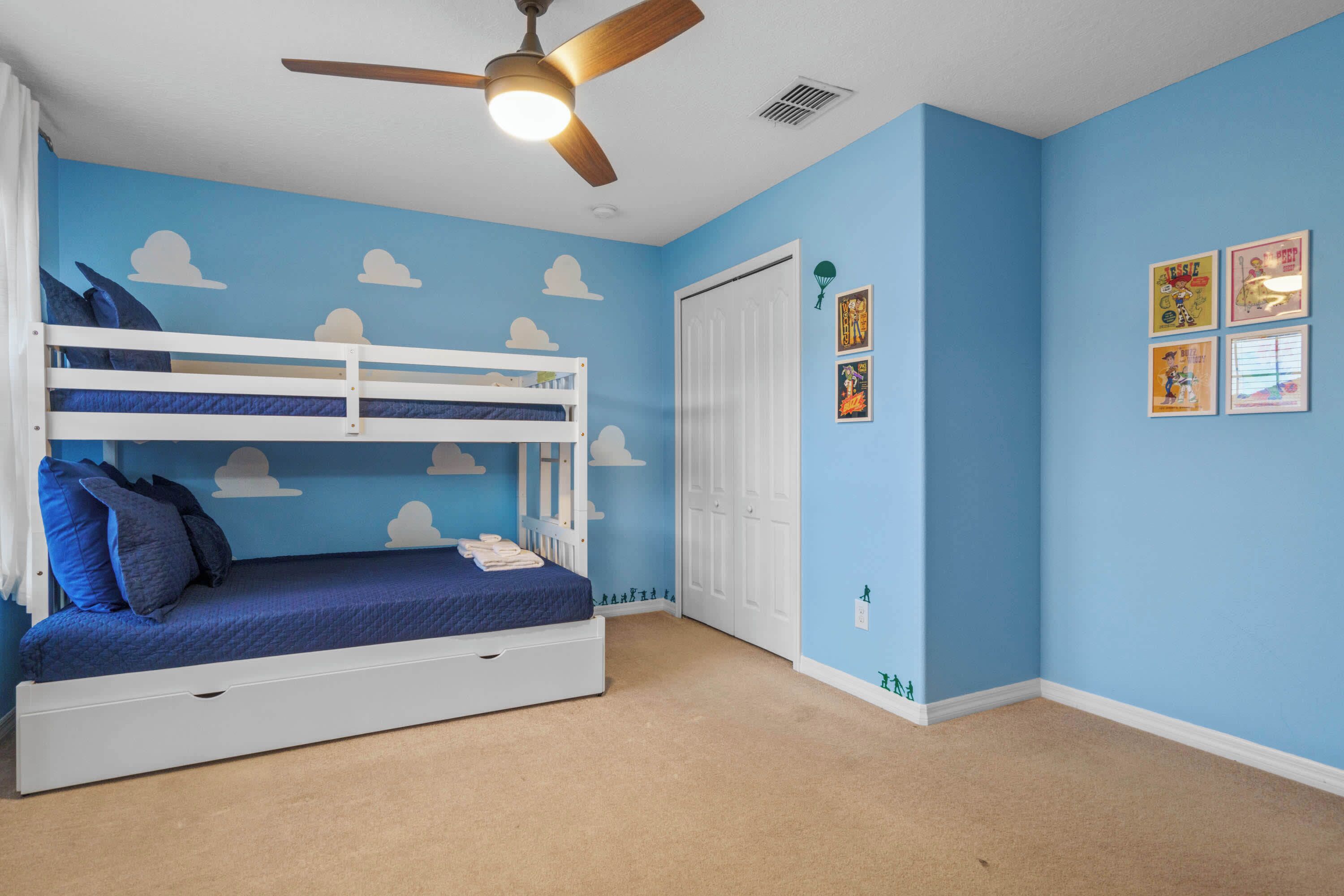 A room with a bunk bed, a ceiling fan, a door, and wall decorations.