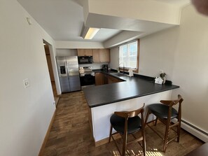 A modern kitchen with a central island, wooden bar stools, and a built-in oven.
