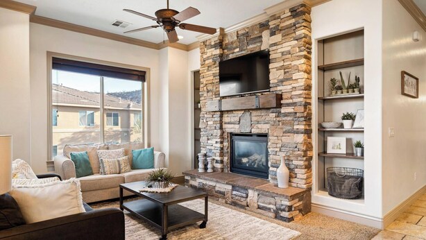A living room with a stone fireplace, a ceiling fan, and a large window offering a view of the outside. - The View Resort Amenities & Epic Views! (Hurricane)