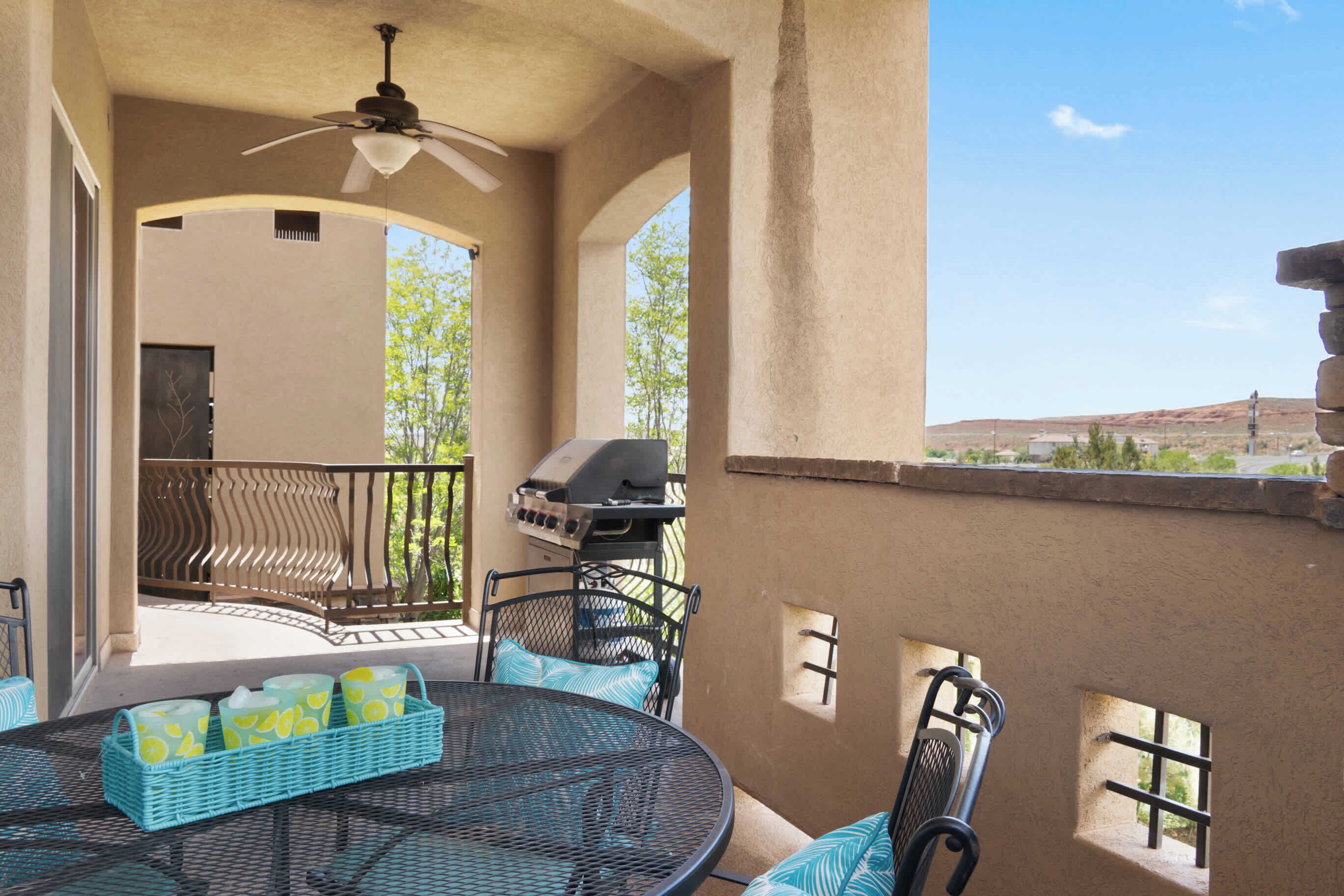 An outdoor patio with a round table, chairs, a grill, and a view of the landscape.