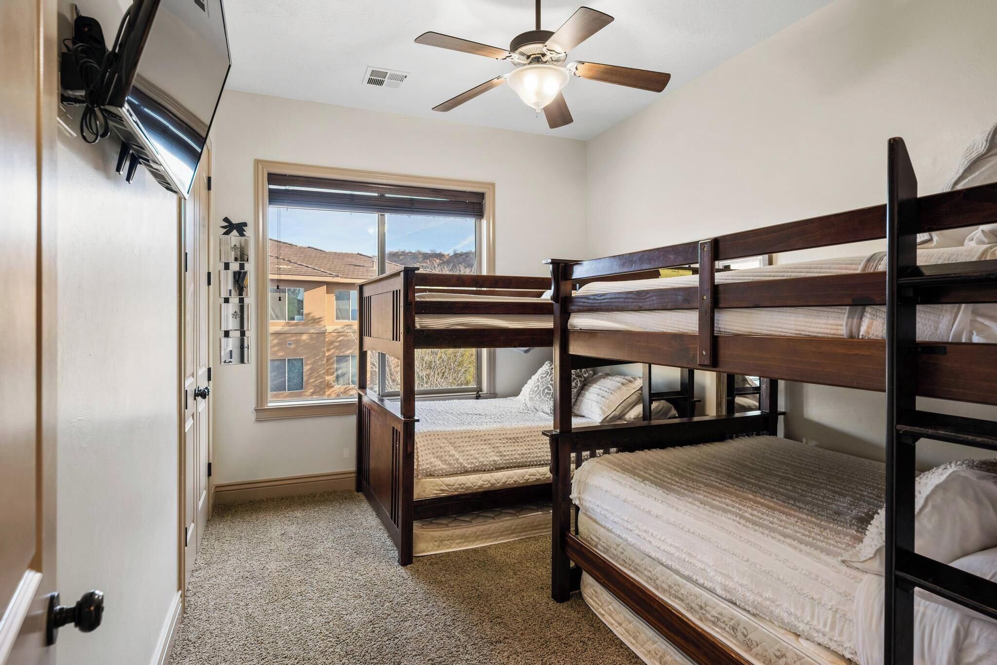 A bedroom with bunk beds, a ceiling fan, a window with a view, and a door with a handle.