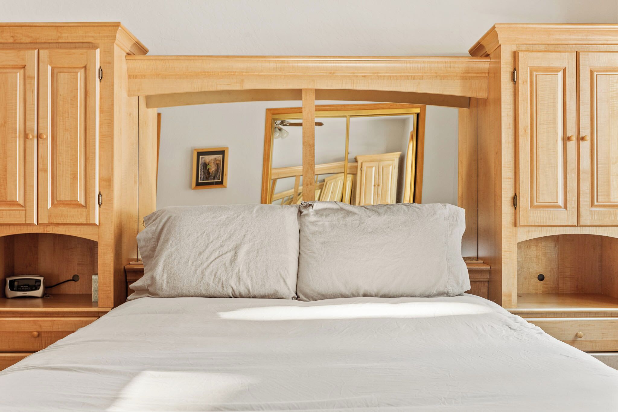 Une chambre à coucher avec un lit, des armoires en bois, une table de chevet et un miroir.